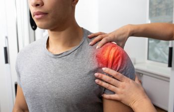 Male athlete suffering from shoulder pain during an appointment with a physical therapist.