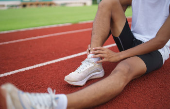 athletes sport man runner wearing white sportswear sitting ankle sprain feeling pain his ankle